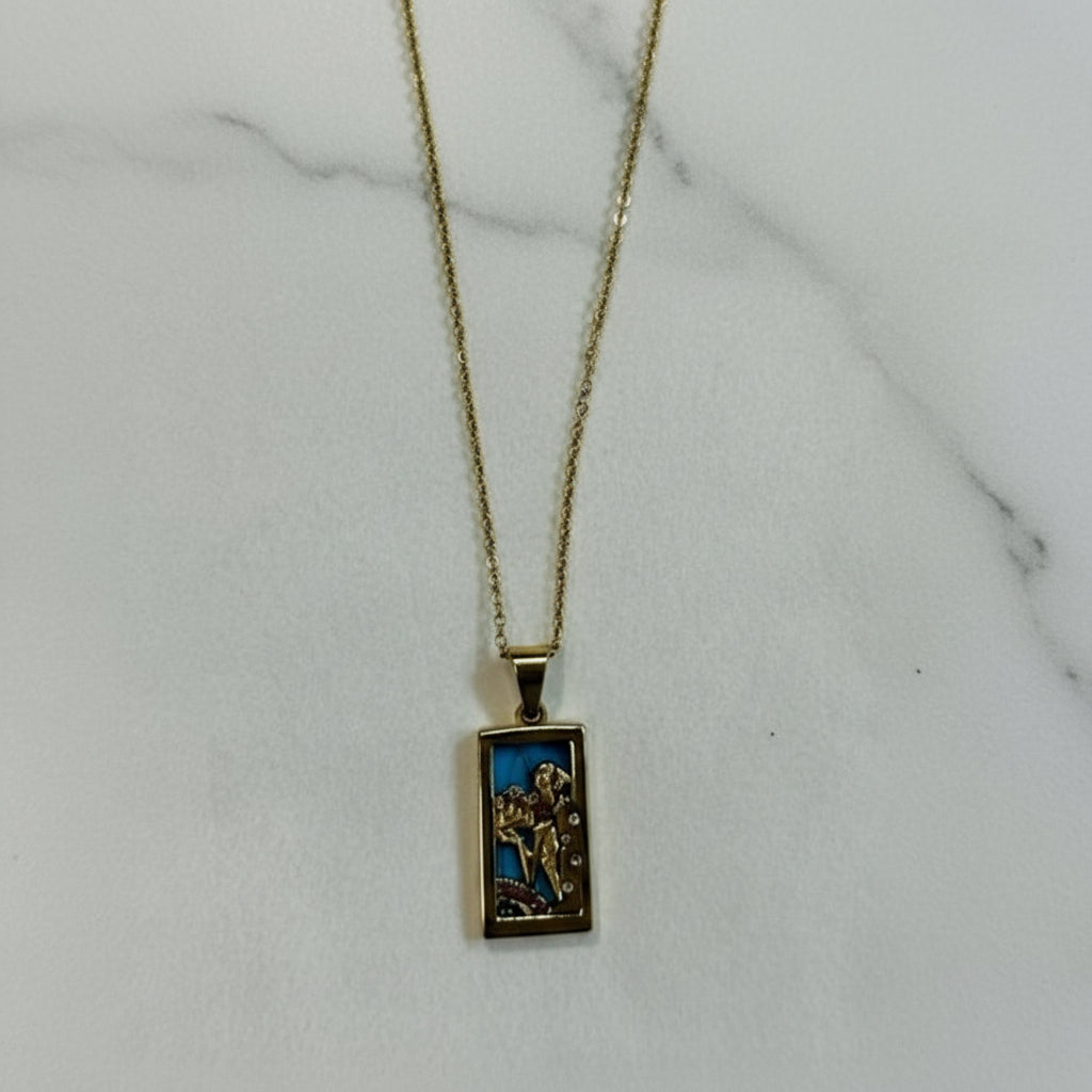 Gold necklace with a rectangular pendant on a marble surface